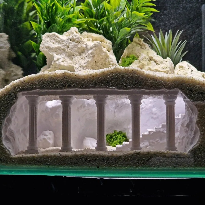 Decorative aquarium scene with white coral, green plants, and a small architectural model.